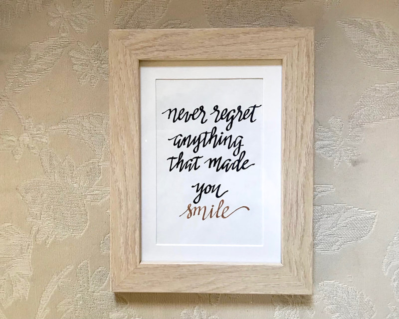 Hand Lettered Calligraphy Quote in black and gold ink "Never regret anything that made you smile"